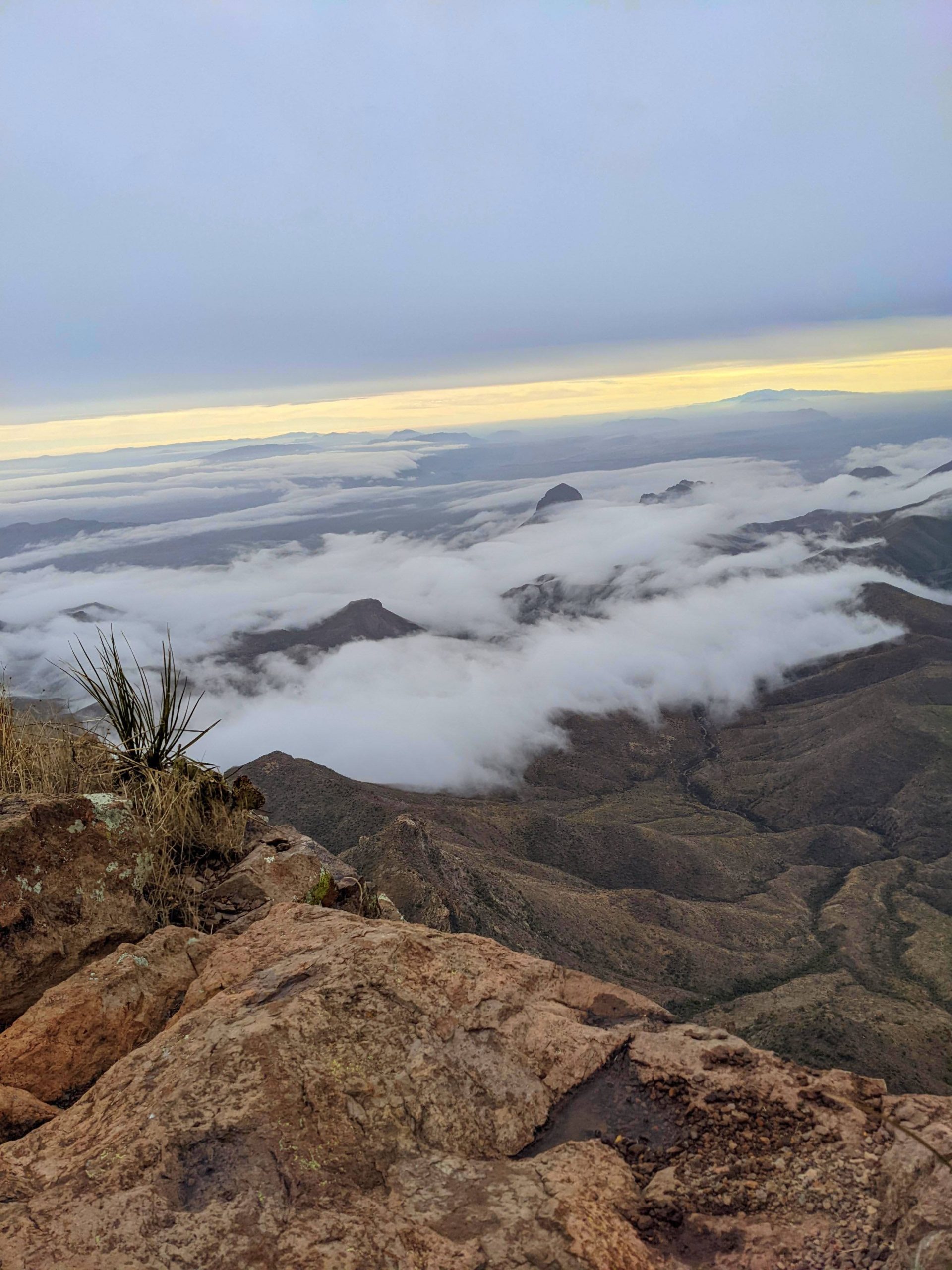 Panoramic view from atop a cliff, looking out over a rugged landscape with low-lying clouds.