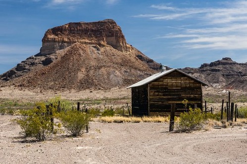 A small wooden barn and corral framed by a mountain butte in the background. These structures were once common in the Big Bend area.