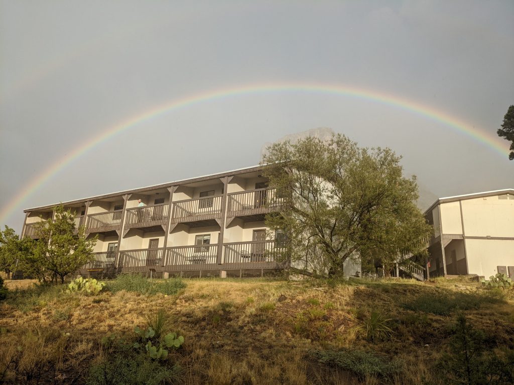 The Chisos Mountain Lodge as viewed from lower down the hill, with a brilliant rainbow visible above it.