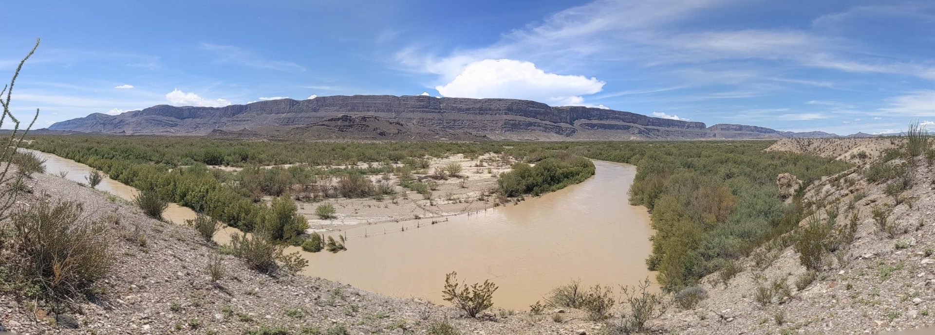 Thr brown waters of the Rio Grande flow past in a panoramic view of the southern Big Bend desert.